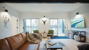 Una sala de estar moderna con un sofá de cuero, sillones verdes, una mesa de centro y un televisor grande en la pared.