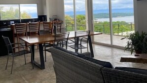Een ruime eethoek met een grote tafel en stoelen, een bank en uitzicht op de oceaan door grote ramen.