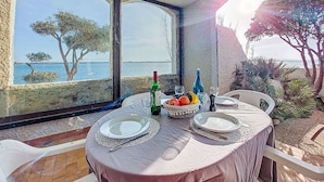 Una mesa dispuesta con platos, una botella y fruta, con vistas a la costa, árboles y un cielo despejado.
