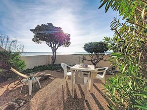 Un patio con una mesa, sillas, un pequeño árbol y vistas a la playa.