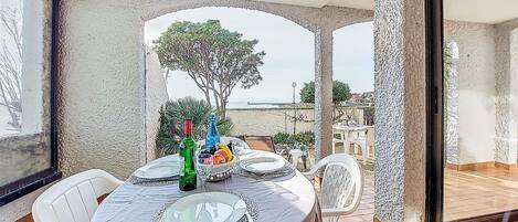A dining area with a table set for two, a view of the beach, and a large window.