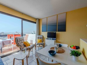 A modern living room with a balcony, a dining table, and a TV mounted on the wall. - Palmyra by Interhome (Le Barcarès)