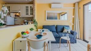 A compact living space with a kitchenette, a dining area with a table and chairs, a sofa, and a large window with curtains.