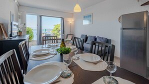 Un comedor con una mesa dispuesta para cuatro personas, un sofá, un refrigerador y vistas al mar.