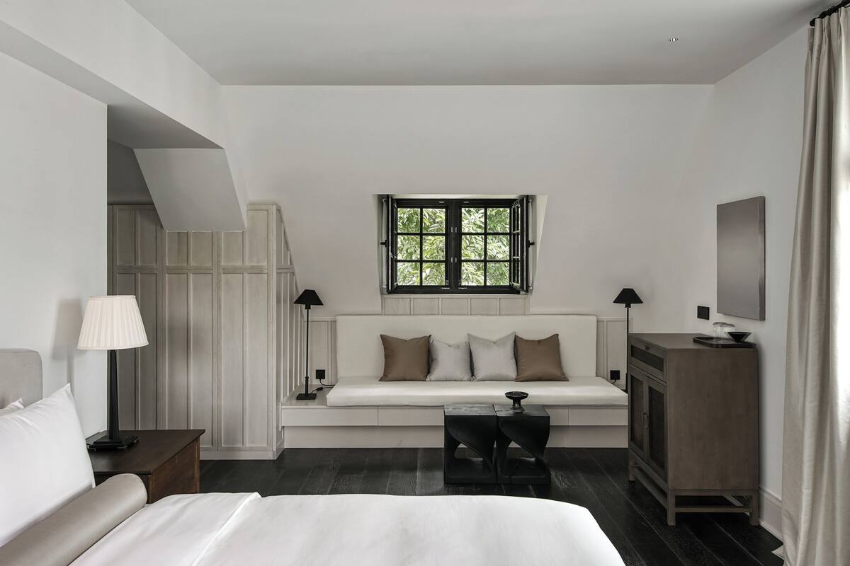 Une chambre d’hôtel moderne dotée d’un grand lit, d’un canapé, d’une petite table, d’une télévision et d’une fenêtre donnant sur des arbres.