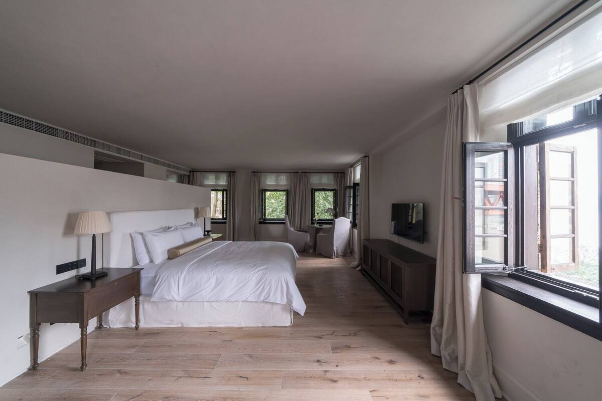 Une chambre d’hôtel moderne, dotée d’un grand lit, d’un bureau, d’une chaise, d’une télévision et d’une fenêtre avec des rideaux.