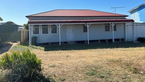 Une maison de plain-pied avec un toit rouge et des murs extérieurs blancs, dotée d’un porche couvert et d’un petit jardin à l’avant.