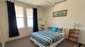 Une chambre à coucher avec un lit, des rideaux, un ventilateur de plafond, un tableau et une table de chevet.