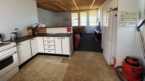 Une cuisine de taille réduite avec des meubles blancs, un plan de travail noir et un plafond en bois. On y trouve un réfrigérateur, un évier et un aspirateur rouge.