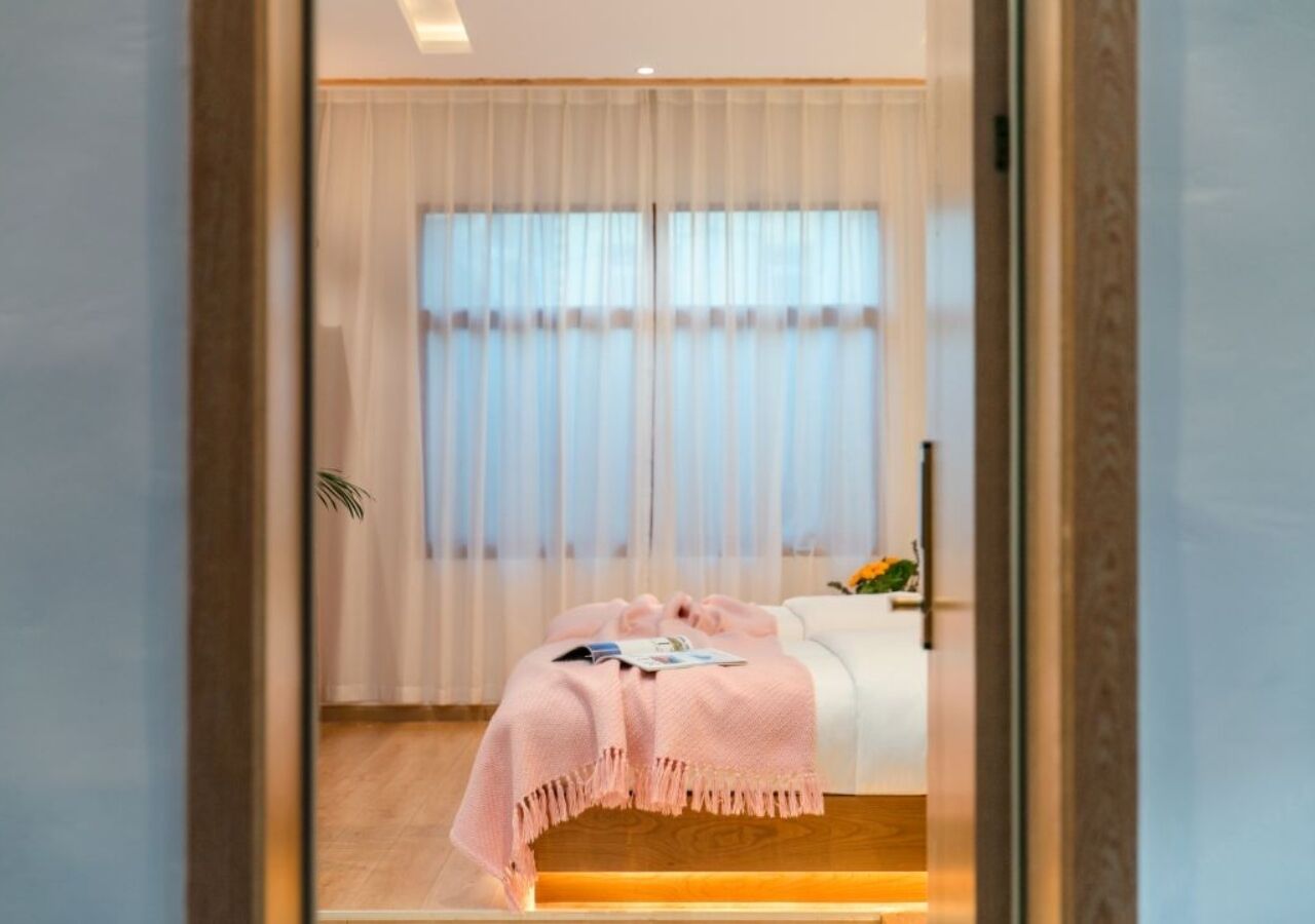 A bedroom with a bed, a bedside table, and a window with sheer curtains.
