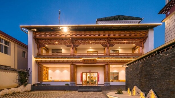 A two-story building with a traditional architectural style, featuring a balcony on the upper floor and a well-lit entrance. - Yunyin Sanqiu Inn (Deqin)