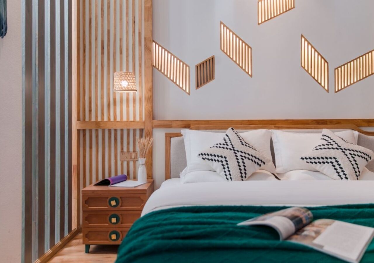 A bedroom with a bed, a nightstand, a wall-mounted light fixture, and a decorative wall panel.