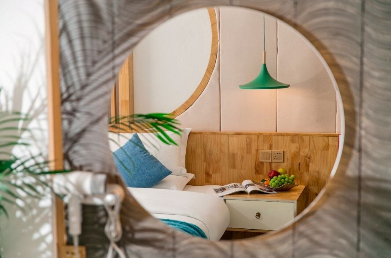 A bedroom with a wooden headboard, a green pendant light, a bedside table with a fruit bowl, and a magazine.