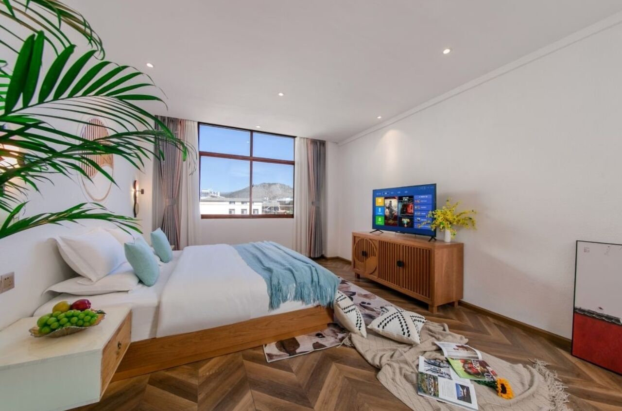 Ein modernes Hotelzimmer mit einem großen Bett, einem Holzkopfende, einem Fernseher, einer Holzkommode und einem großen Fenster mit Blick auf die Stadt.