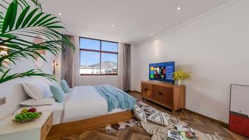 Ein modernes Hotelzimmer mit einem großen Bett, einem Holzkopfende, einem Fernseher, einer Holzkommode und einem großen Fenster mit Blick auf die Stadt.
