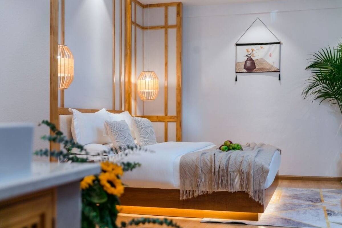 Un dormitorio moderno con una cama, lámparas de noche, una obra de arte en la pared y una planta en maceta.
