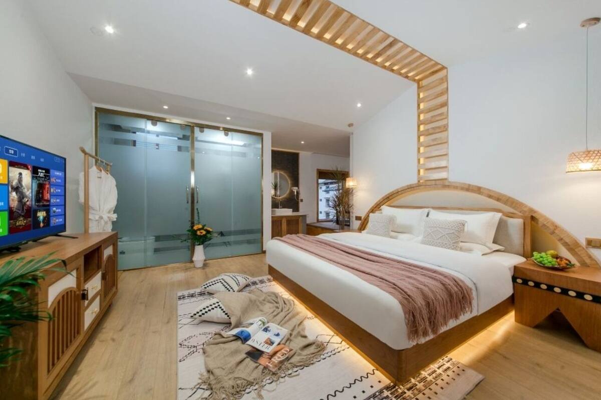 Un dormitorio moderno con una cama grande, mesitas de noche, un televisor y una puerta de vidrio que da al baño.