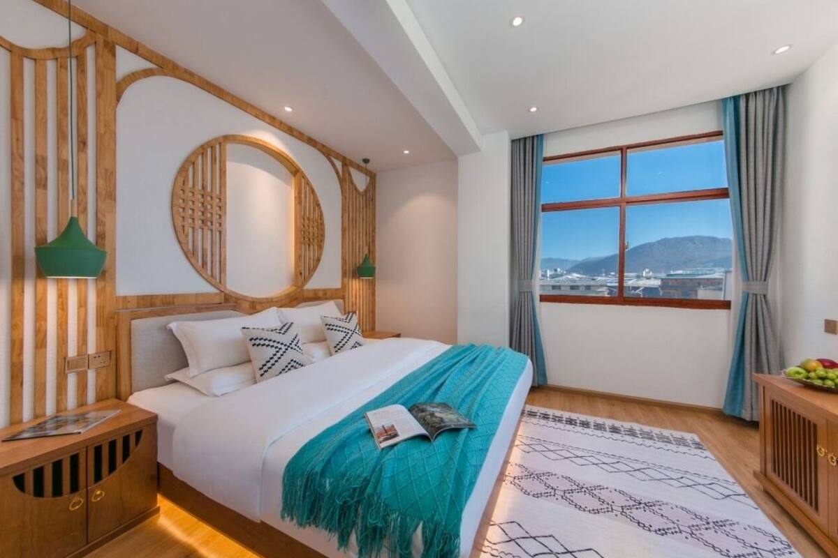 Una habitación de hotel moderna con una cama grande, cabecera de madera, un ventanal con vistas y una mesita de noche de madera.