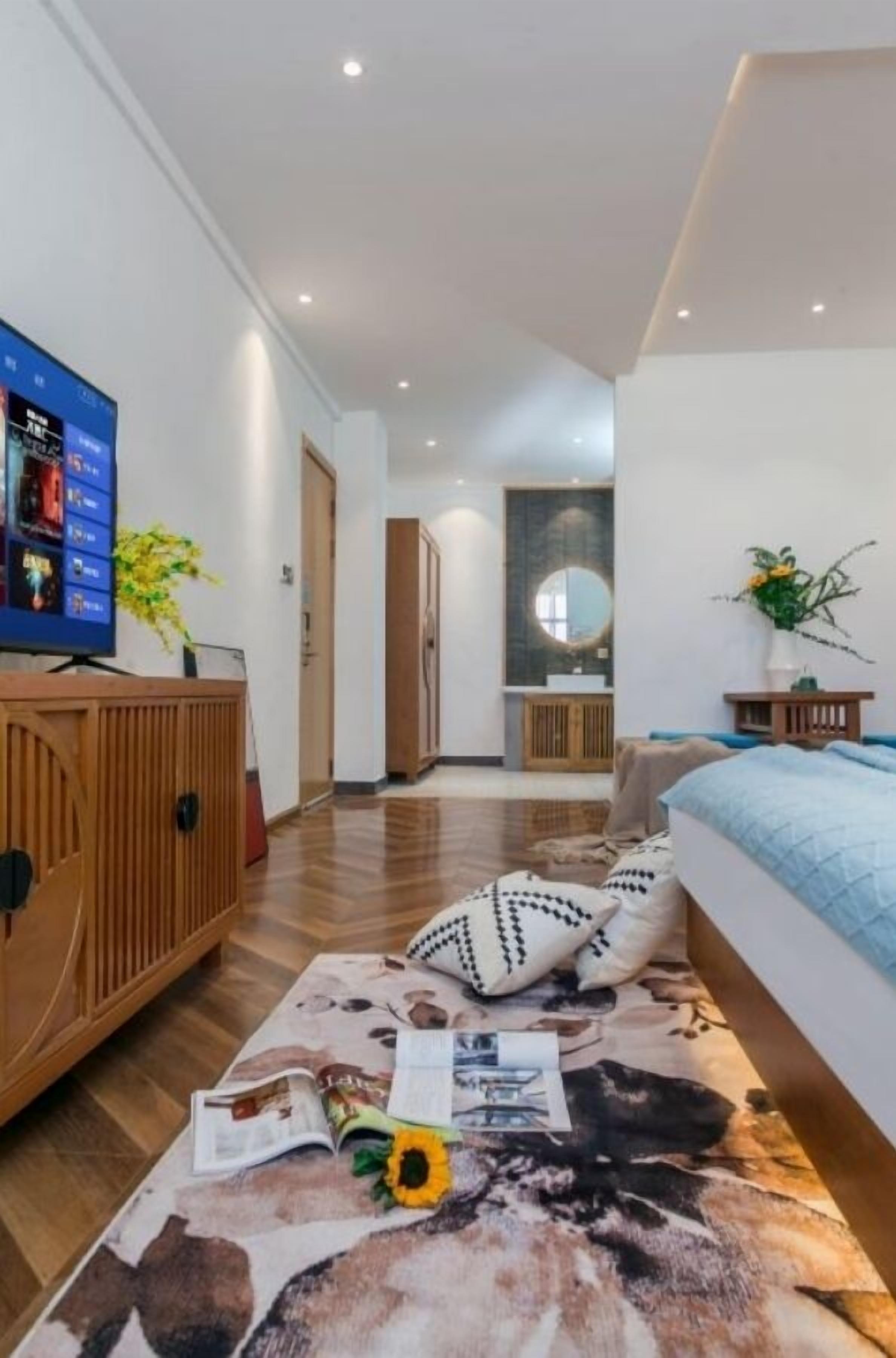 A modern hotel room with a wooden cabinet, a bed with a blue headboard, a flat-screen TV on a wooden stand, and a large mirror above the bed.