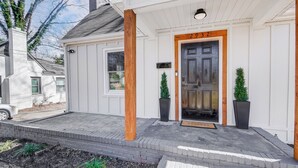 A white building with a dark door, two potted plants, and a mailbox. - Hot Tub + Big Yard • Minutes from Uptown! (Charlotte)