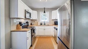 A modern kitchen with white cabinets, stainless steel appliances, a central island with a stove, and a large refrigerator. - Hot Tub + Big Yard • Minutes from Uptown! (Charlotte)