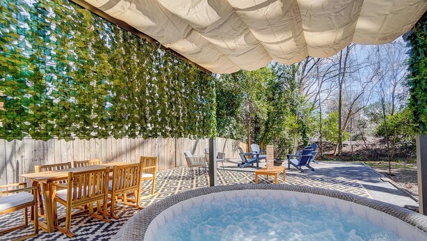 A hot tub surrounded by outdoor furniture, a wooden table, and chairs. - Hot Tub + Big Yard • Minutes from Uptown! (Charlotte)