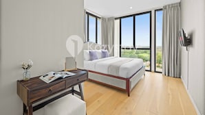 Une chambre moderne avec un grand lit, un bureau et une vue sur la ville grâce à de grandes fenêtres.