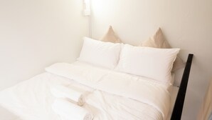 A neatly made bed with white bedding and pillows, a black headboard, and a white wall with a light switch. - Code Hostel at Kampong Glam (Singapore)