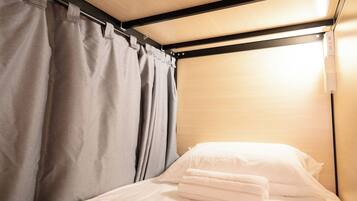 A single bed with white linens and a grey curtain, a wooden headboard, and a light fixture above.