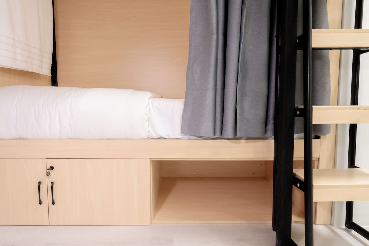 A bunk bed with a wooden frame, a pull-out desk, and a wardrobe with two doors.