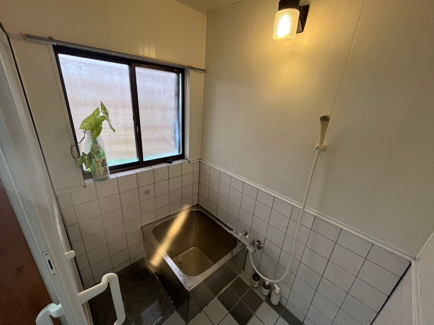 A small bathroom with a window, a shower, and a sink.