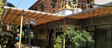 Un espacio al aire libre cubierto con mesas y sillas, una planta en maceta y un edificio de diseño moderno.