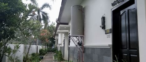 Un sendero que lleva a un edificio con una puerta negra, un tanque de agua y un cartel.