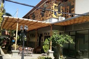 Een overdekt terras met stoelen en tafels, een pergola en een gebouw met een geometrisch gevelontwerp.