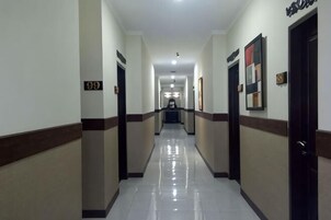 Un pasillo de hotel con puertas numeradas 99 y 100, un suelo pulido y obras de arte enmarcadas en las paredes.