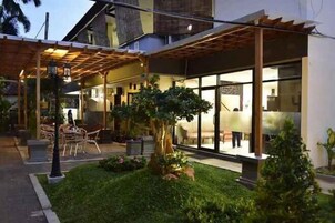 Un edificio moderno con una zona de estar cubierta al aire libre, un amplio ventanal y un jardín cuidado.