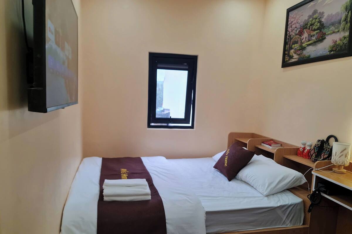 A hotel room with two beds, a small desk, a window, and a painting on the wall.