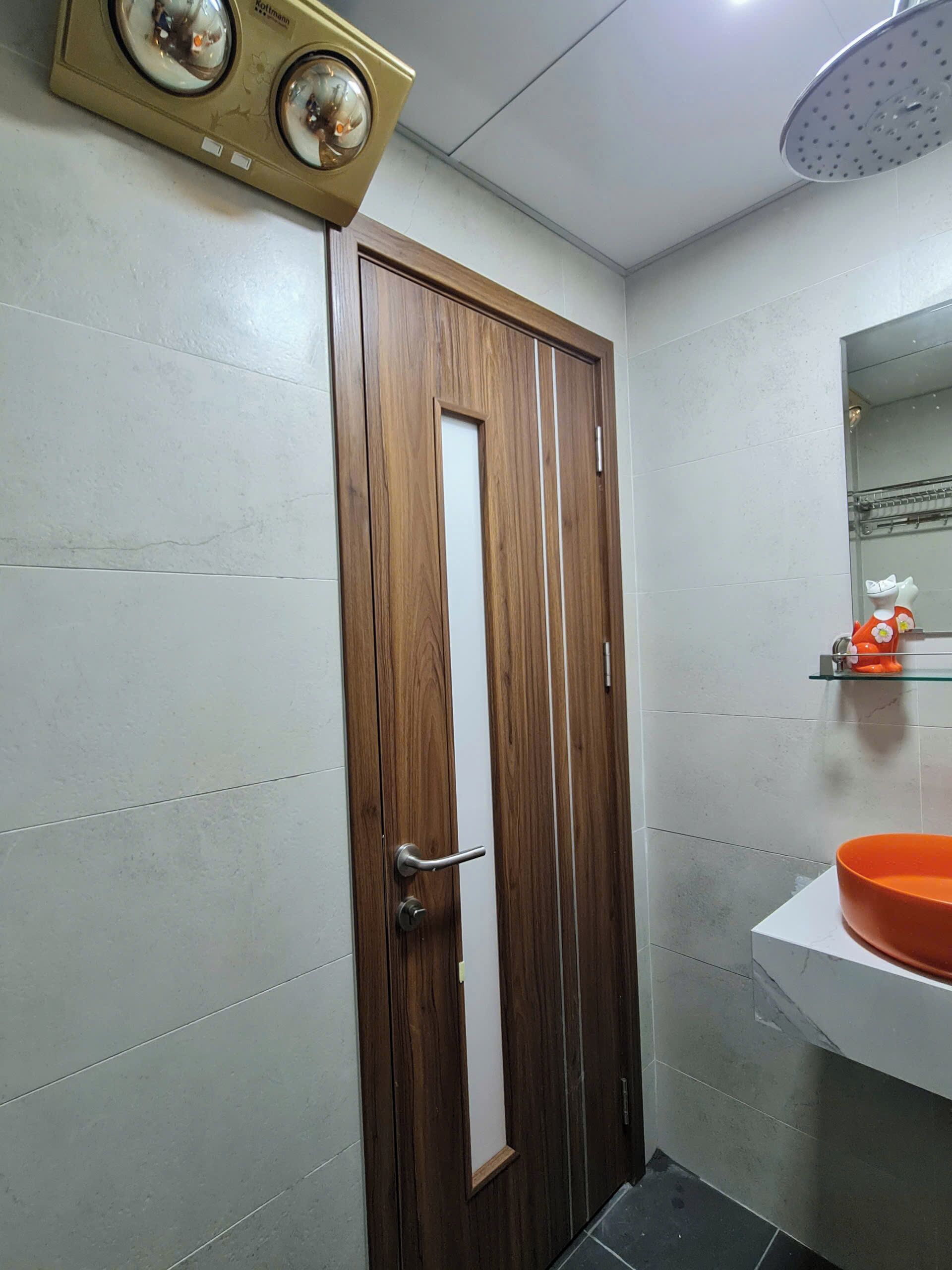 A bathroom with a wooden door, a white sink with an orange basin, and a shower with a circular head.