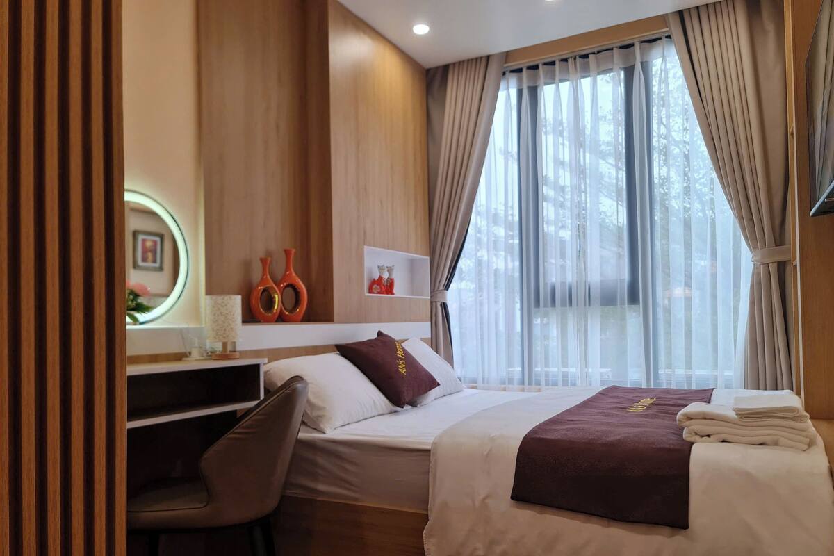 A hotel room with a bed, a desk, a chair, a round mirror, and a window with curtains.