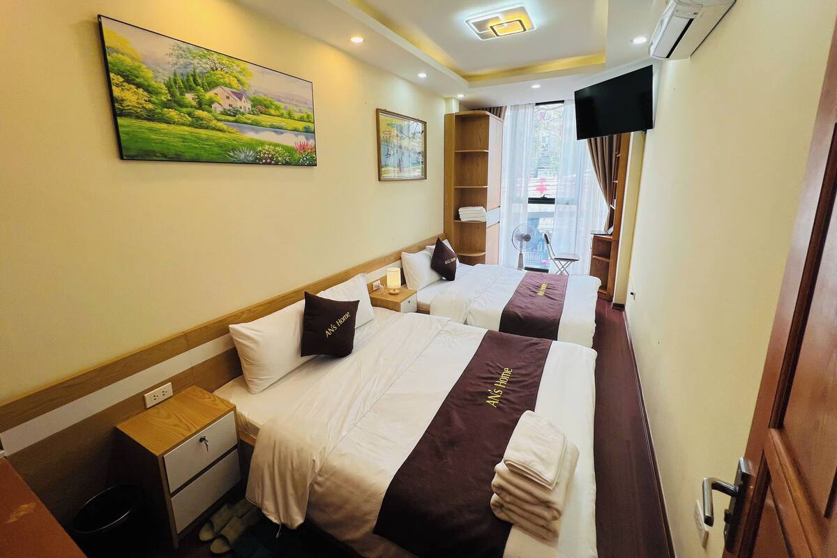 A hotel room with two beds, a painting, a TV, and a window with a view.