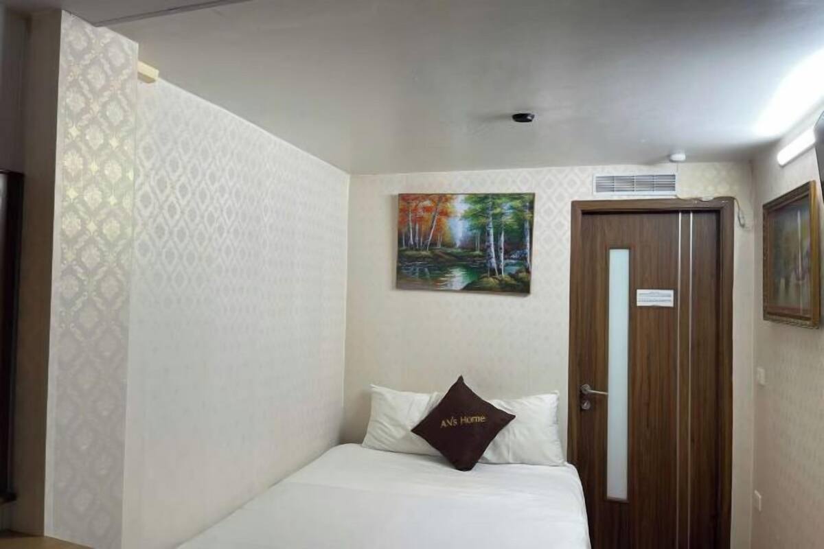 A hotel room with a bed, a painting, a wooden door, and patterned wallpaper.