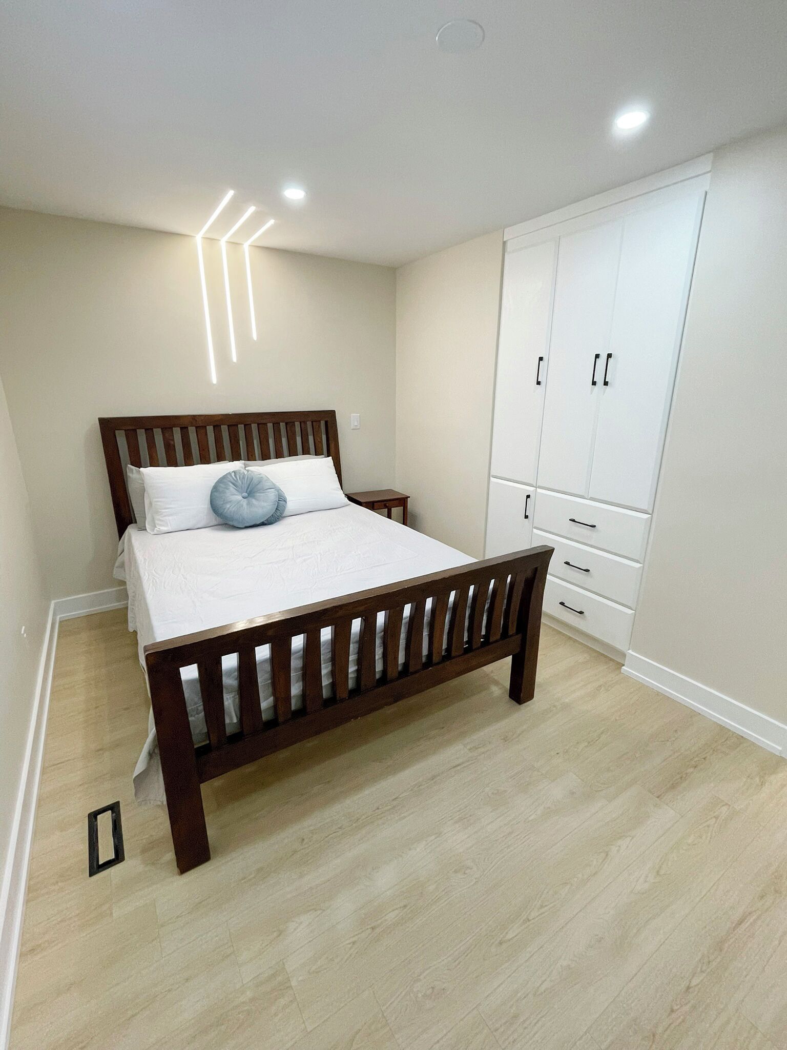 A bedroom with a wooden bed, white bedding, a small bedside table, and a wardrobe with multiple drawers.