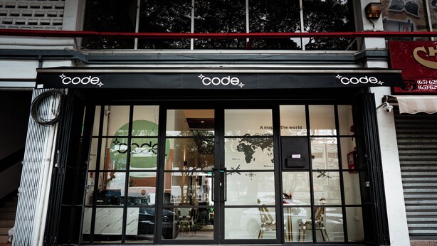 A storefront with a black awning and glass doors, featuring a world map and a sign that reads "code." - Code Hostel at Lavender (Singapore)