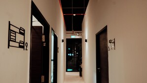 A corridor with doors labeled with numbers and a ceiling with exposed pipes and lighting fixtures. - Code Hostel at Lavender (Singapore)