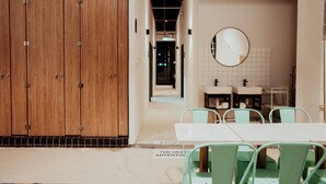 A modern hotel lobby with wooden lockers, a dining area with a white table and green chairs, and a large mirror on the wall. - Code Hostel at Lavender (Singapore)