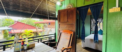 A room with a wooden table, a chair, a bed with a blue curtain, and a green wall.