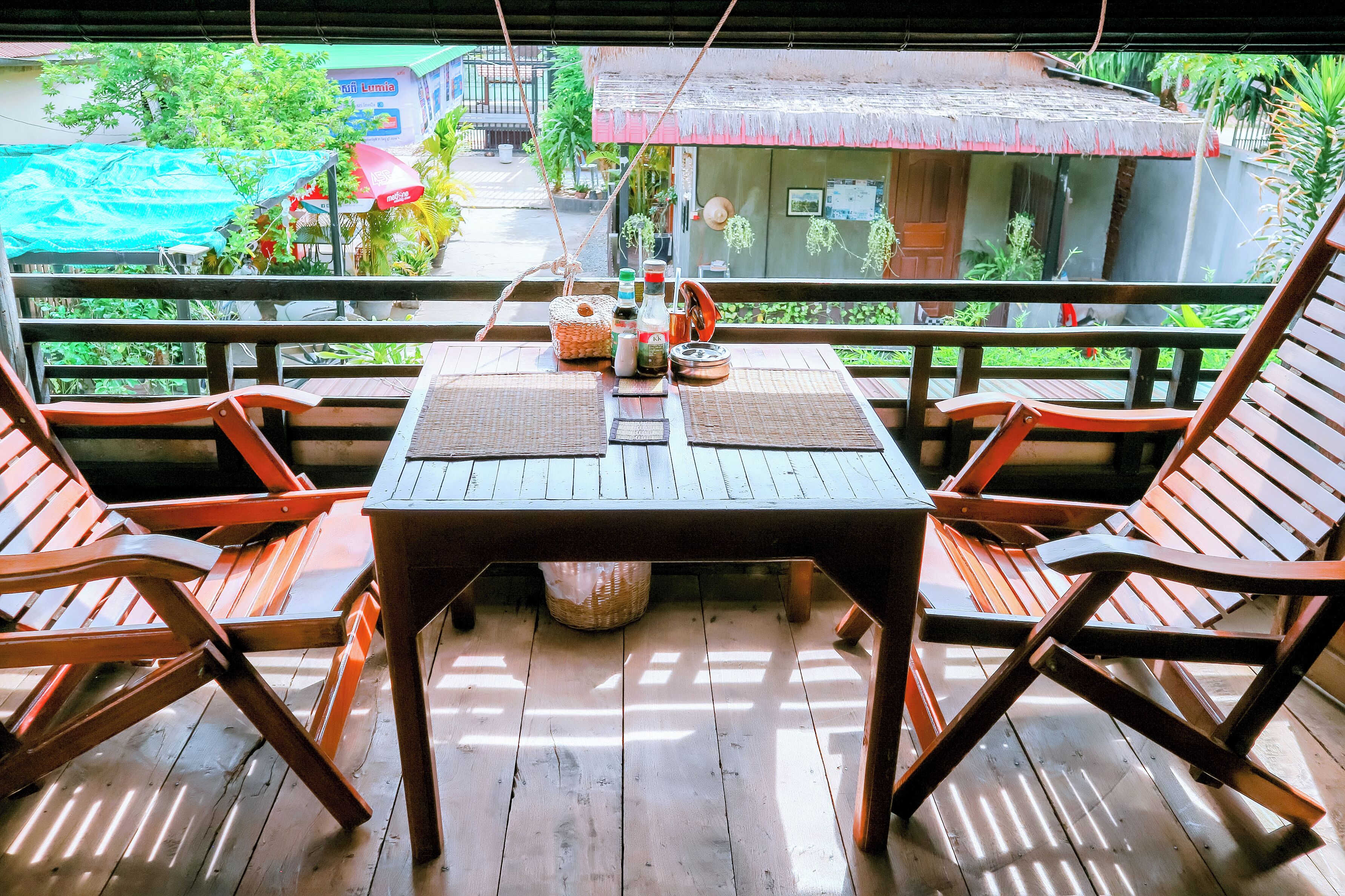 A wooden table with two chairs on a balcony with a view of a house and greenery.