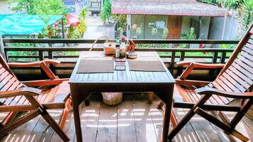 A wooden table with two chairs on a balcony with a view of a house and greenery.