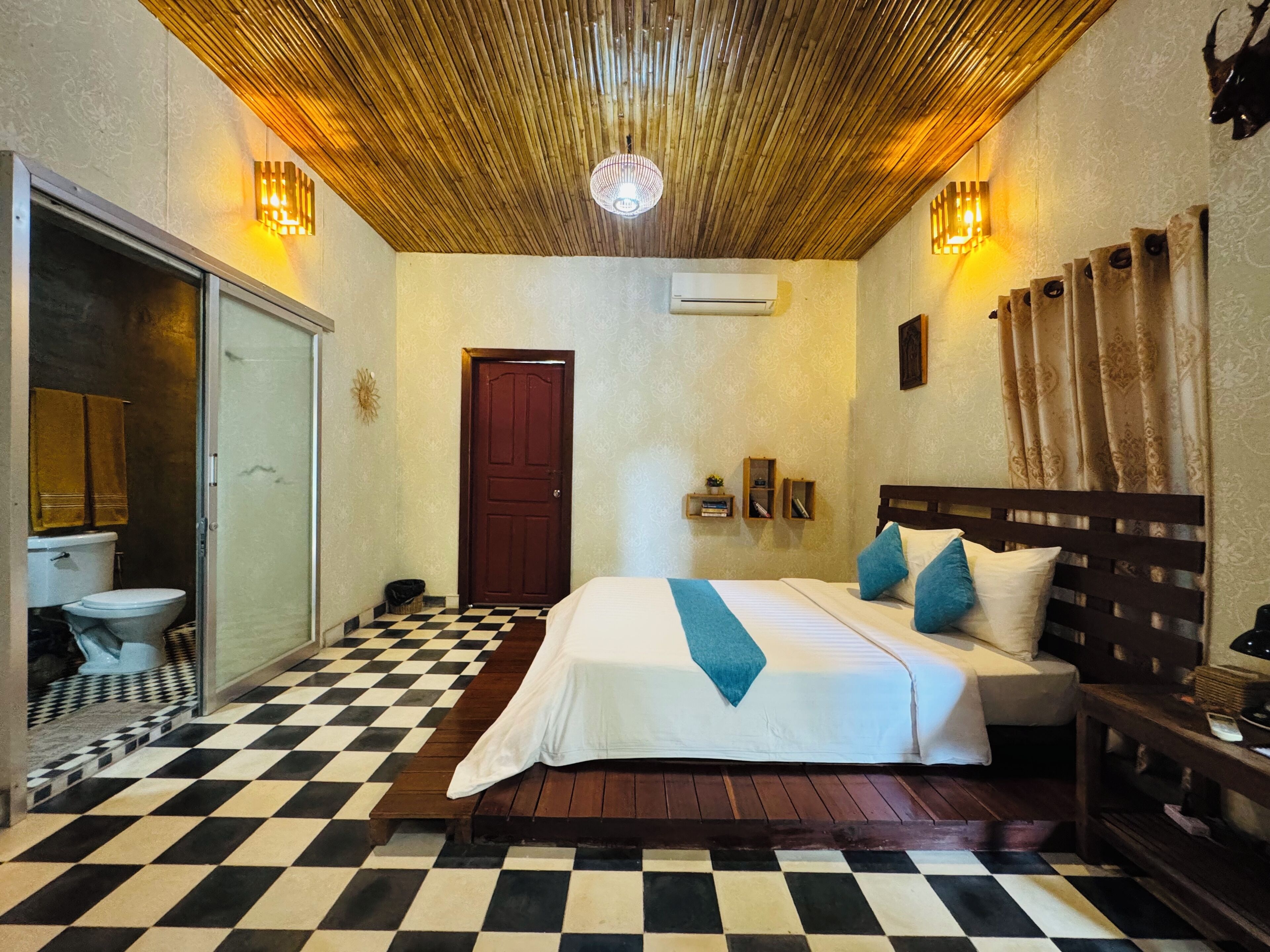 A hotel room with a checkered floor, a bed with blue and white bedding, a wooden headboard, and a wall-mounted air conditioner.