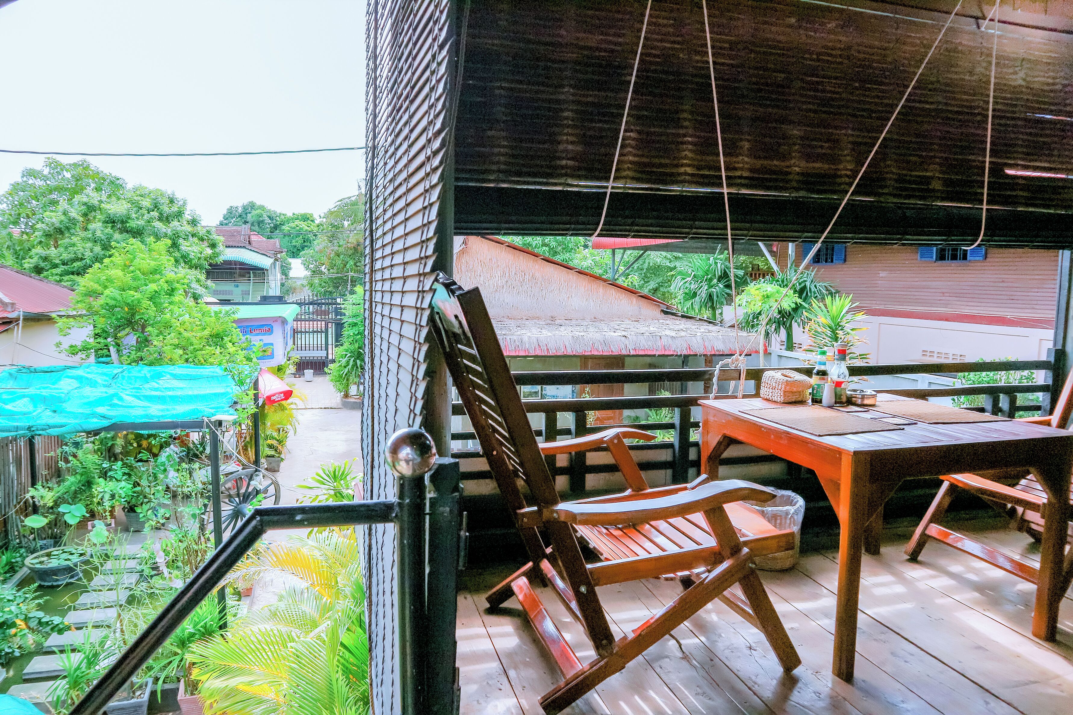 A wooden deck with a table and chairs, surrounded by potted plants and a view of a street.